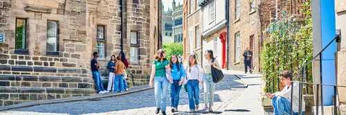 A group of four female students walk down a cobbled Durham street