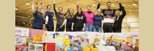 A group of staff volunteers cheering behind a large amount of food