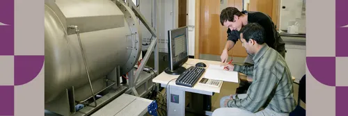 Two male researchers working at a computer with machinery in front of them