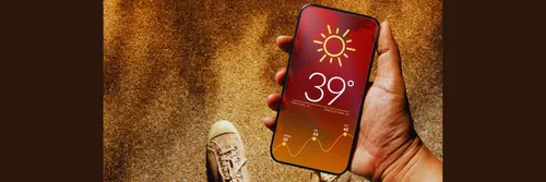 A person standing on sand holds a phone showing a high temperature.