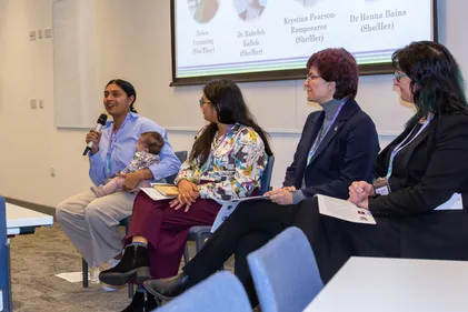 Four women in engineering, one holding microphone and cradling baby, sitting on a panel discussing engineering