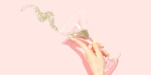 A picture of a hand holding a martini glass with gold glitter spilling out in celebration