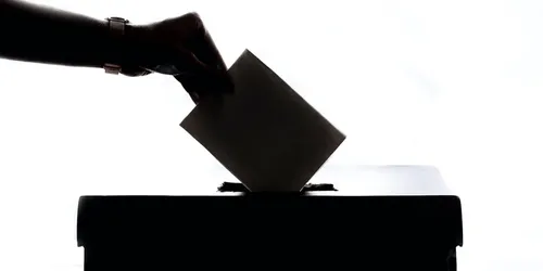 A picture of a hand putting a ballot in a box