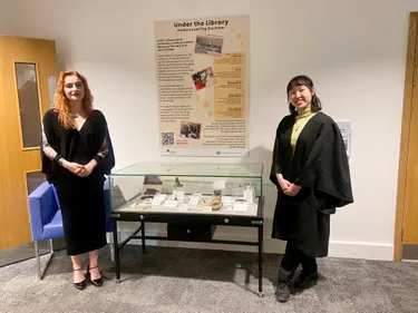 Two students in gowns flank a display case
