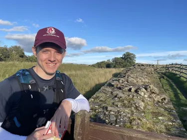 Durham Archaeology alumnus Sam Betley next to Hadrian's Wall