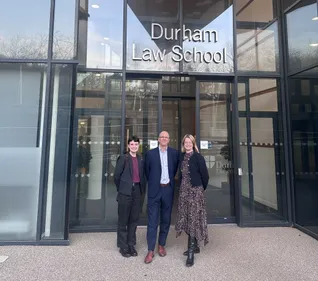 Three people standing outside Durham Law School