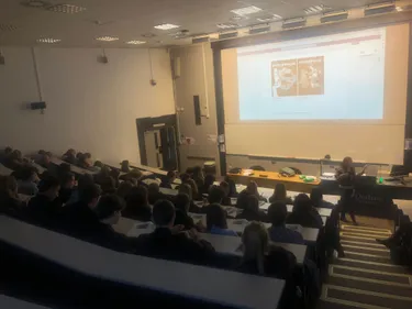 School pupils sitting in a darkened university lecture theatre with screen and lecturer at front