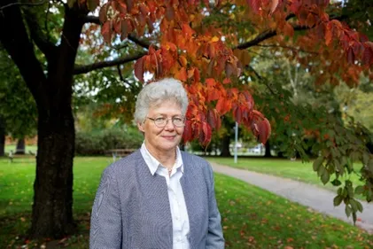 Photo of Anne L'Hullier stood beneath a tree in autumn colours