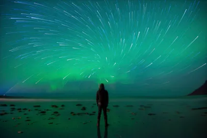 stock photo of person on beach looking up at northern lights