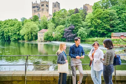 A group of students by a river in front of Durham Cathedral