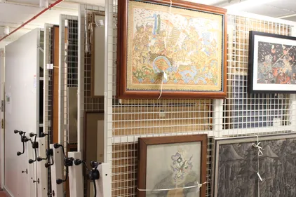 paintings hanging on a series of vertical mesh racks with other cupboards visible behind