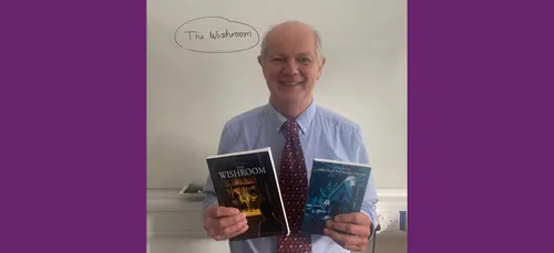 Professor David Waugh standing in front of a whiteboard holding two books he has written.