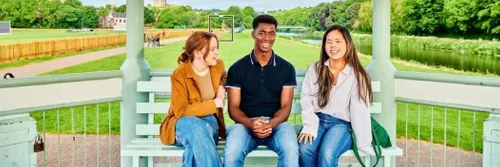 Three students sat on a bench with a field behind them