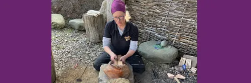 Woman sits on the ground inspecting an artefact on an archaeological site