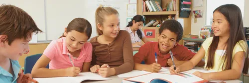 Students sit at a table with books and writing utensils