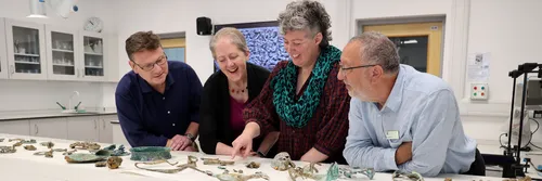 Four colleagues stand at a table with Melsonby artefacts spread around