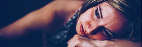 A sad woman lies on the floor with her fist under her face.