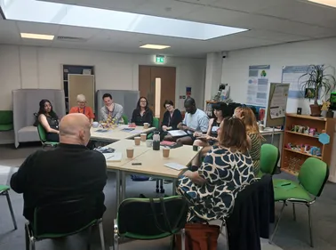 Photograph of a group of people sitting in discussion in an academic institution's room.