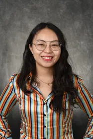 Portrait of an asian female with glasses, long, dark hair, and a colourful, striped shirt with a grey background