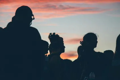 Dark silhouettes of three people against the sunset.