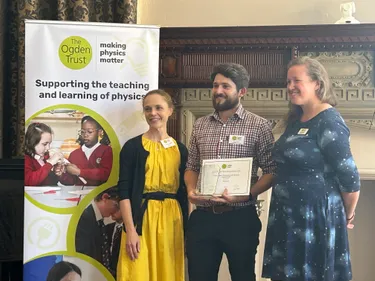 female in yellow dress and male with beard in checked shirt collecting an award made from glass from a second female