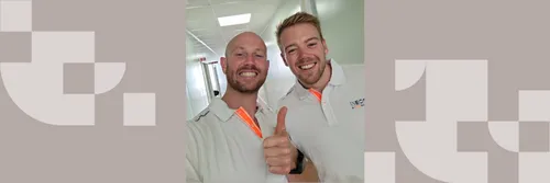 Two men wearing white polo shirts standing together grinning at the camera making a thumbs up sign
