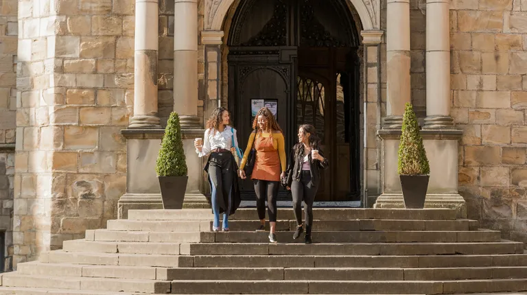 3 students walk down stairs at castle