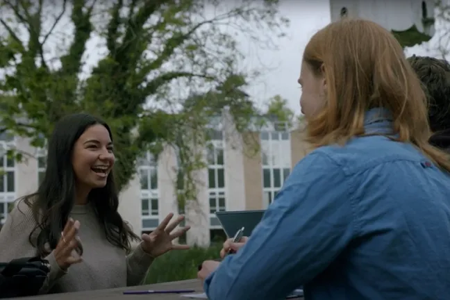 A student talks to two other students at a picnic table