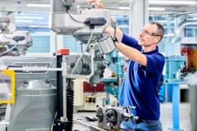 Man in blue t-shirt, wearing a protective visor over his eyes, uses a piece of engineering equipment