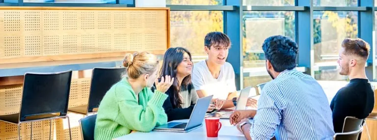 Group of students in discussion in boardroom with laptop