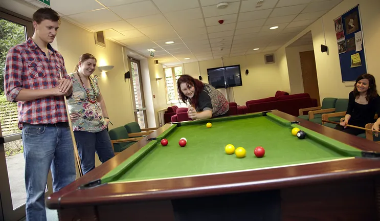 A mixed group of students playing pool in a modern common room.