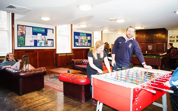 Students playing foosball, pool and sitting around chatting in a student common room