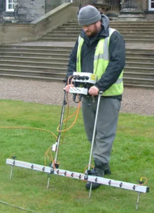 an archaeologist conducting an earth electrical resistance survey on the lawn of a stately home