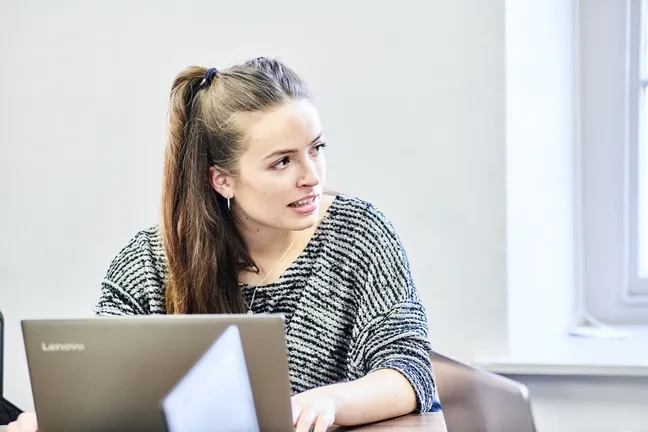 A student working at a laptop and contributing to a discussion