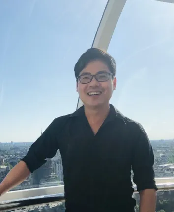 Man in black shirt smiles with blue sky behind him