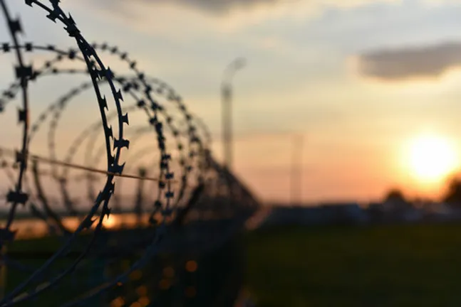Close up of barbed wire on a prison wall, with grass and sunset in background