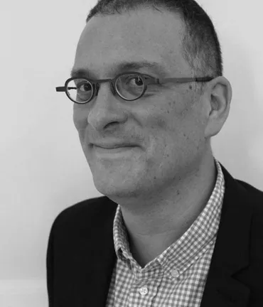 A headshot of Cobus van Staden smiling in black and white