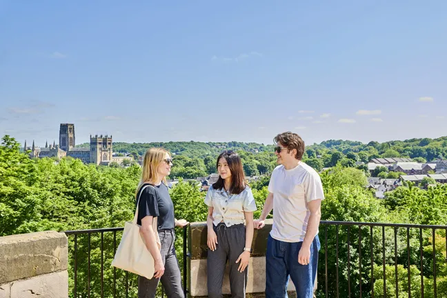A group of three students stood in front of a view over Durham with Durham Cathedral in the background