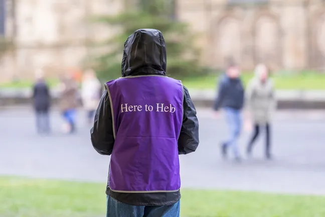 Person in a black coat with the hood up and a purple Durham University 