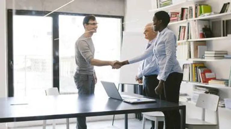 Two people shaking hands in an interview at a desk in an office