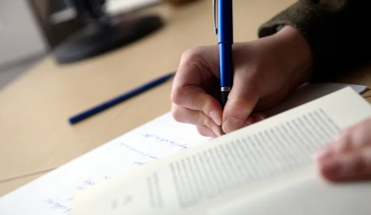 A person making notes from a textbook