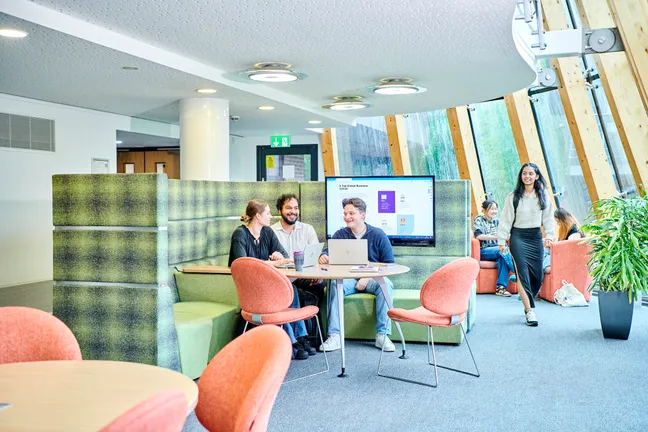Groups of postgraduate students sit in a modern, airy study space