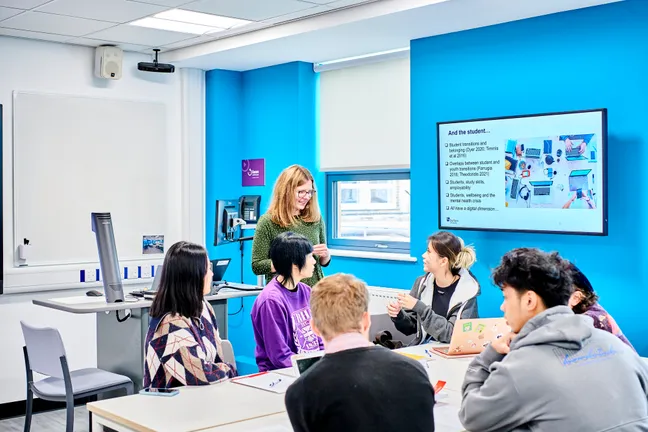 Academic in green dress discussing research with students who are sat at a table