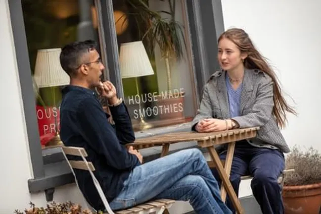 Male and female student chatting at a table outside a coffee shop