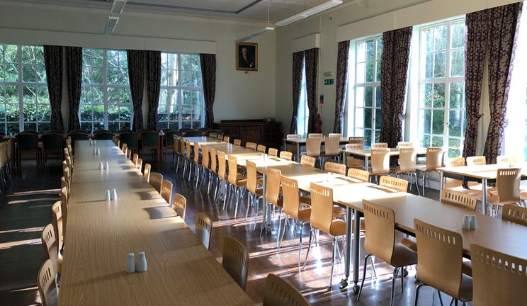 Sun shining through Cuth's dining room with rows of tables and chairs and thick drape curtains at the windows.
