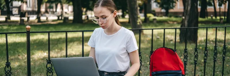 Young woman student searching jobs online with laptop outdoors