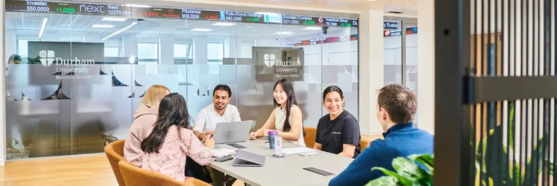 Students smiling around a table in Durham University Business School in front of a Bloomberg terminal