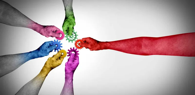 A photograph of six different coloured hands joining small cogs together
