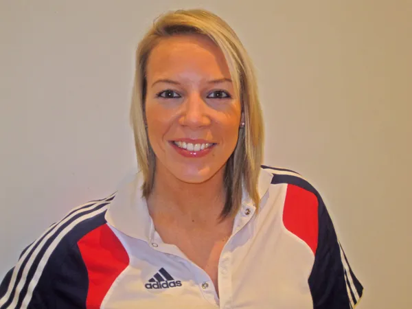 A blonde haired woman wearing a sports jacket smiling at the camera