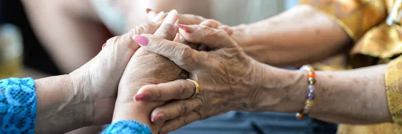 Close up of two older women's hands clasping each other.